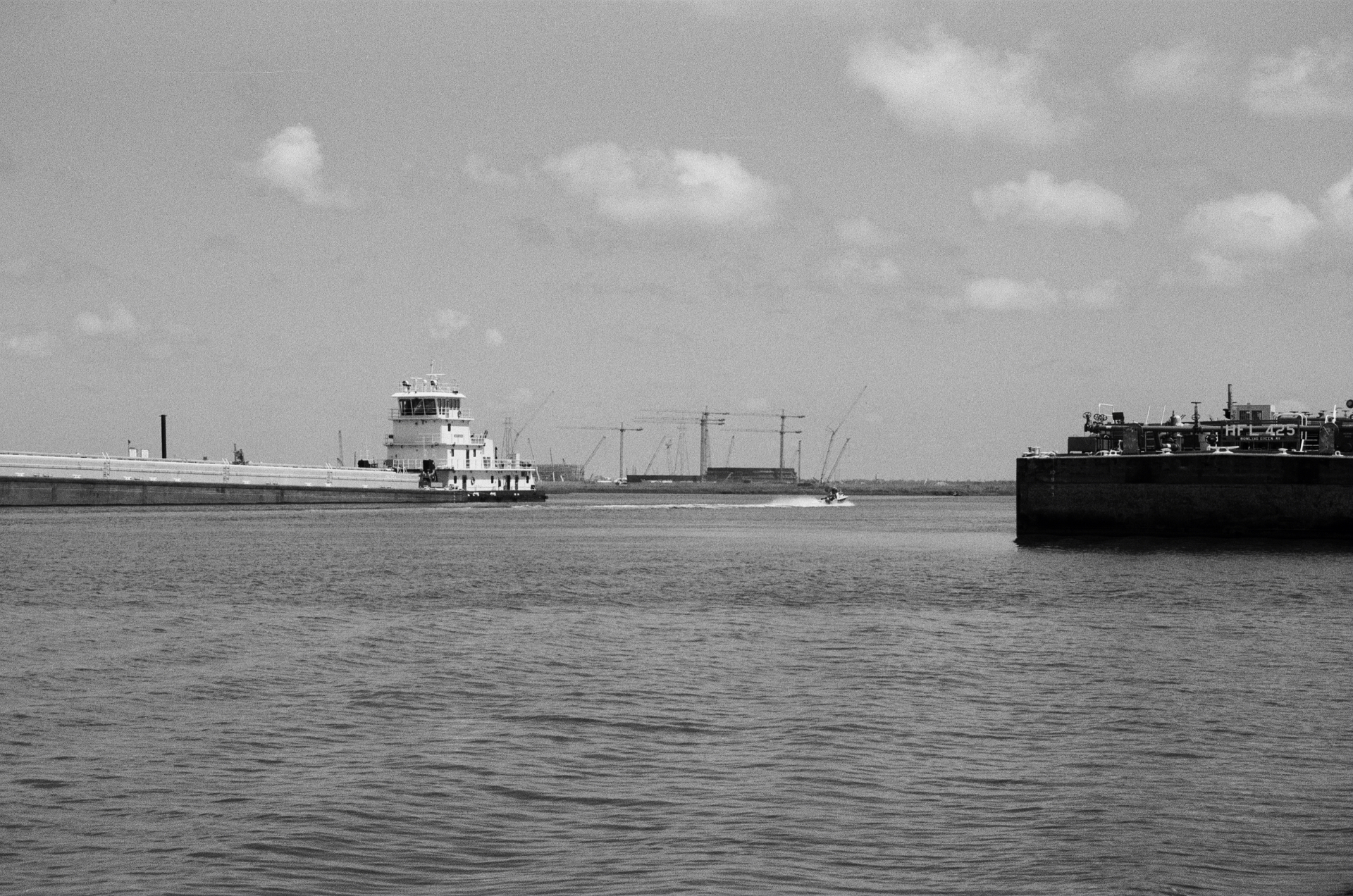 Tugboat and barge on a wide river with industrial cranes in the distance