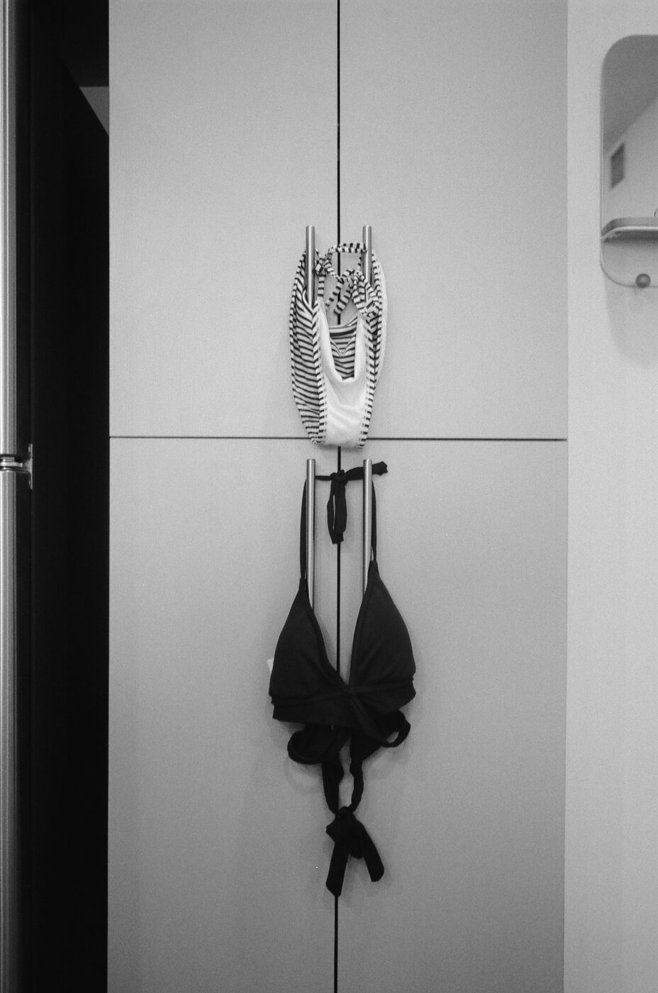 Striped swimsuit and black bikini hanging on cabinet handles
