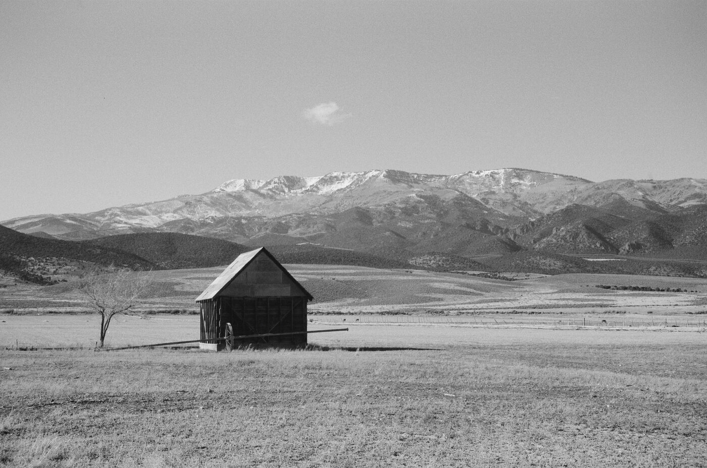 Lone barn in a wide valley with snow-capped mountains