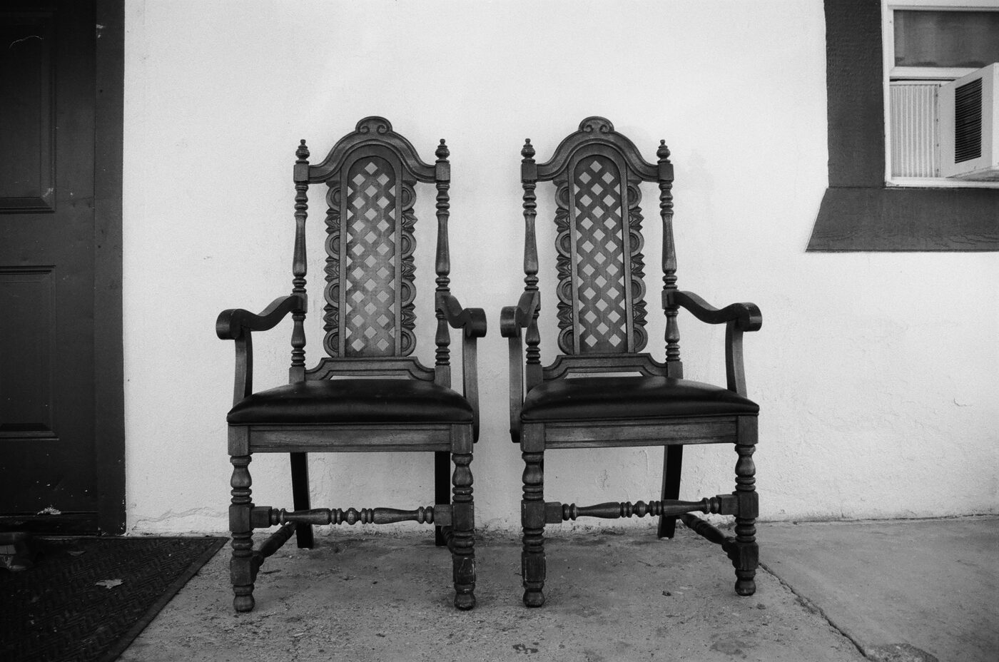 Two ornate wooden chairs against a stucco wall