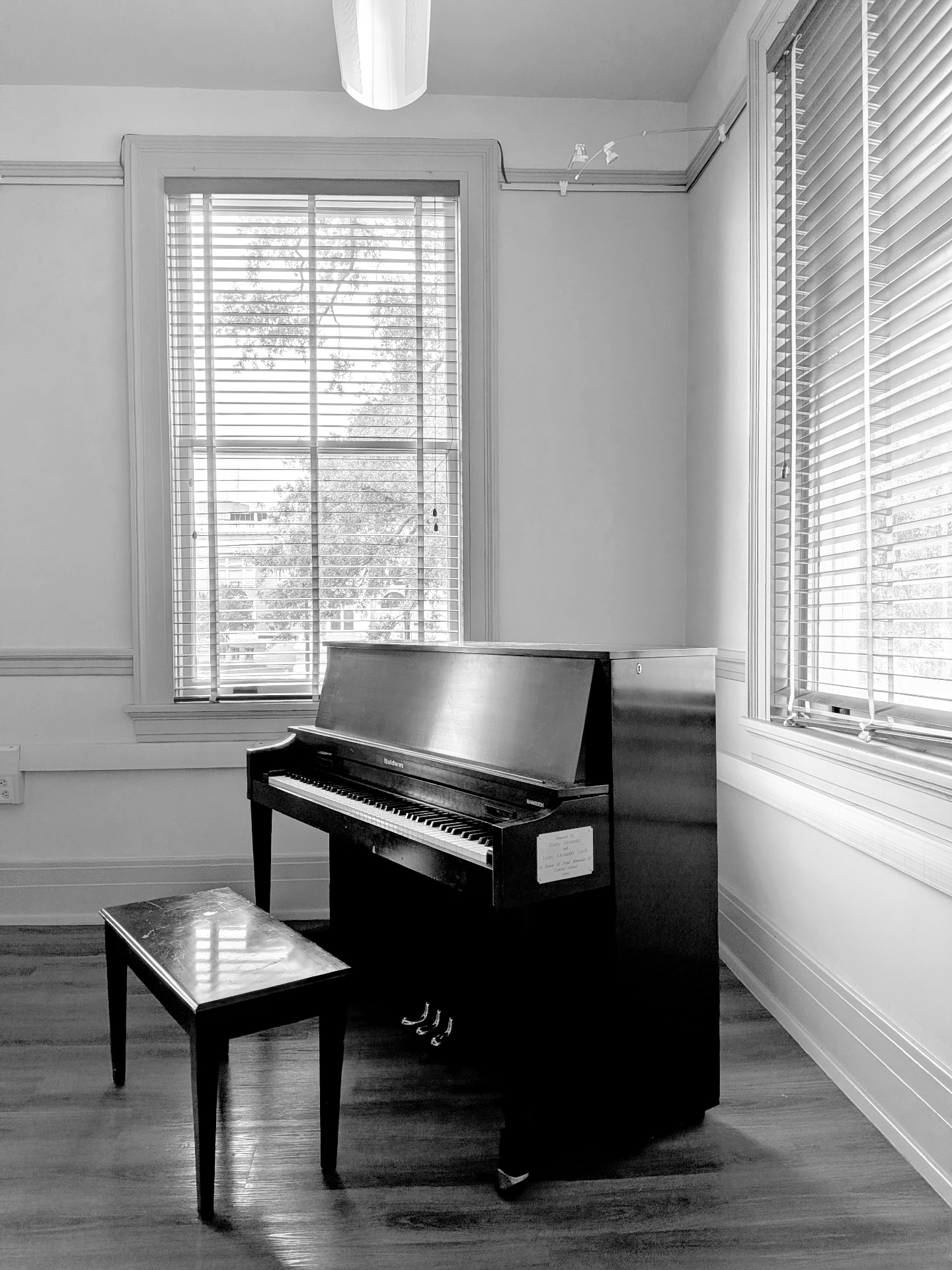Upright Baldwin piano between two sunlit blinded windows