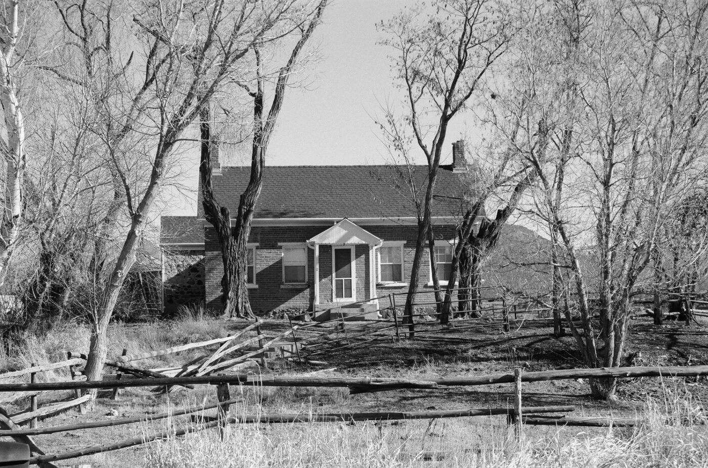 Small house behind bare trees and split-rail fence