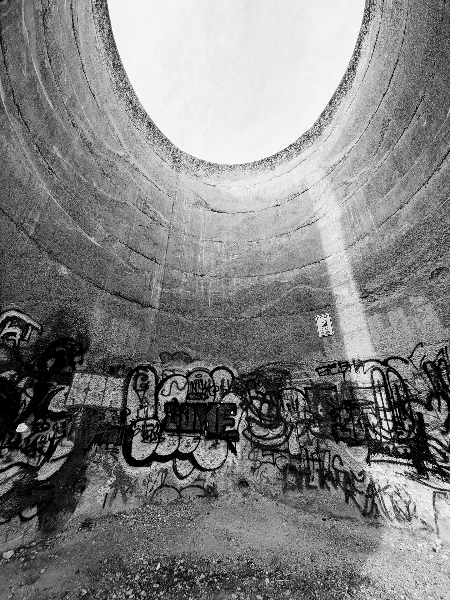 Looking up inside a graffiti-covered concrete silo with open sky